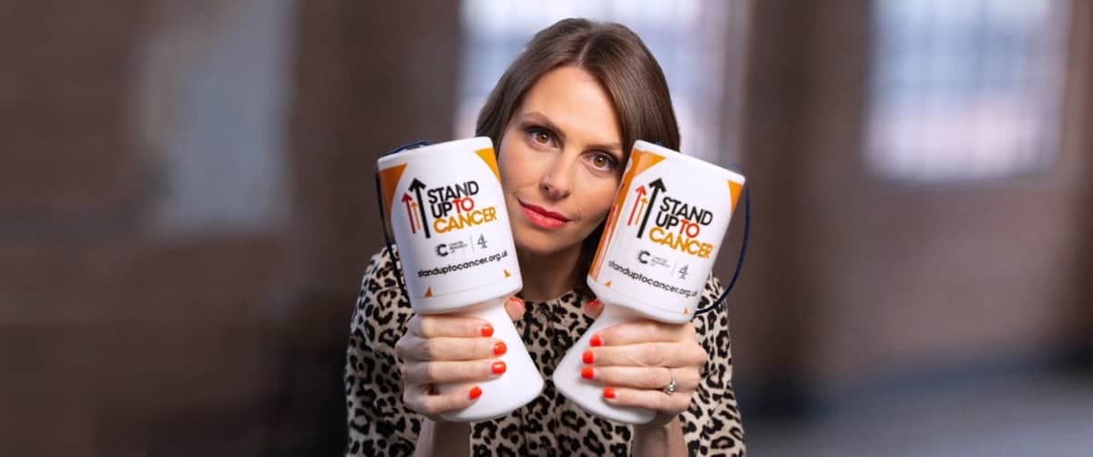 Ellie taylor looking directly at the camera while holding 2 stand up to cancer money pots.