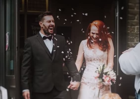 Daniel and becca holding hands leaving their wedding church with confetti flying in front of them.