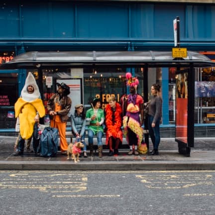 Celebrities dressed in fancy dress at a bus stop.