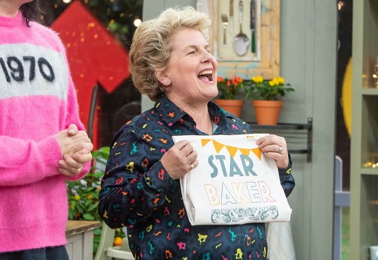 Sandi Toksvig holding a star baker apron mid-cheer.