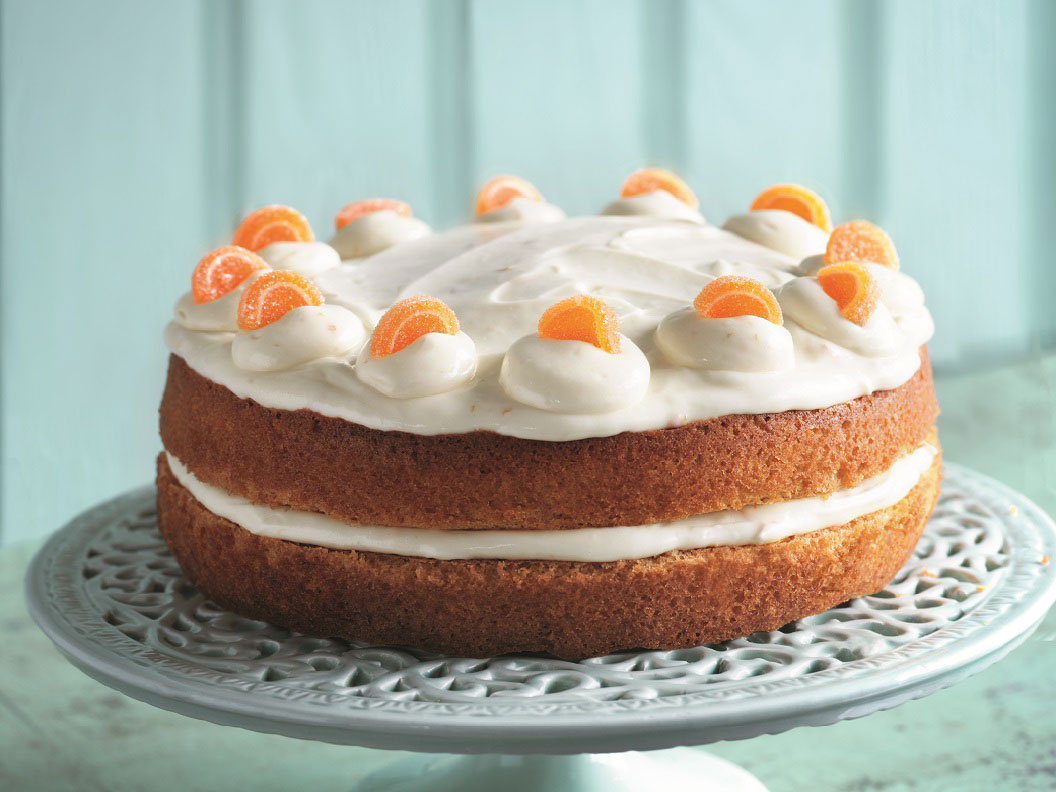 Fresh Orange Cake from recipe booklet, on a cake stand against a blue wall 