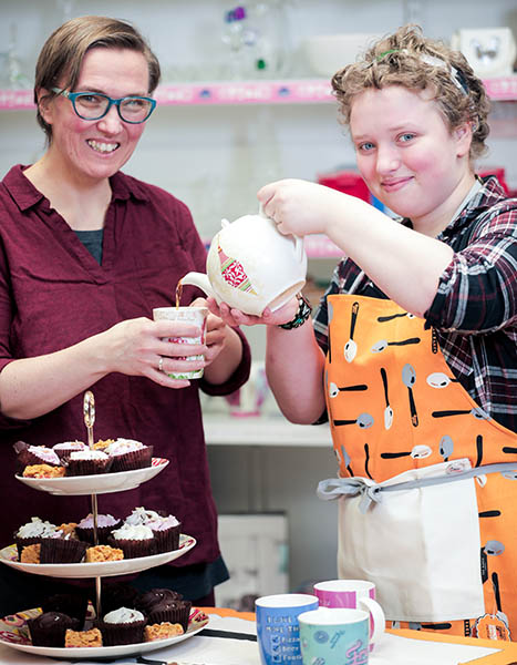 Thirza and Hendrikje pouring tea surrounded by their bake sale food