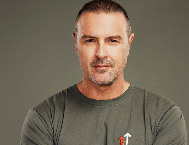 Paddy McGuinness with his arms folded wearing a dark grey Stand Up To Cancer t-shirt