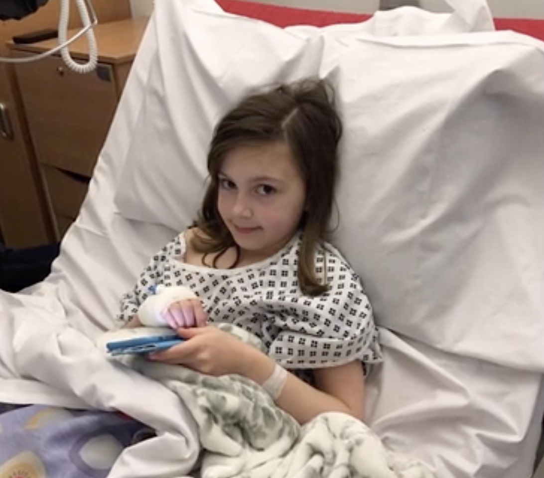 Rebecca lying in a hospital bed, looking at the camera with a little smile