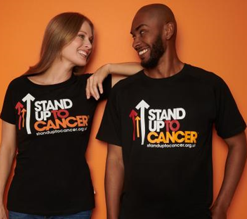 A man and woman facing each other laughing wearing Stand Up To Cancer t-shirts