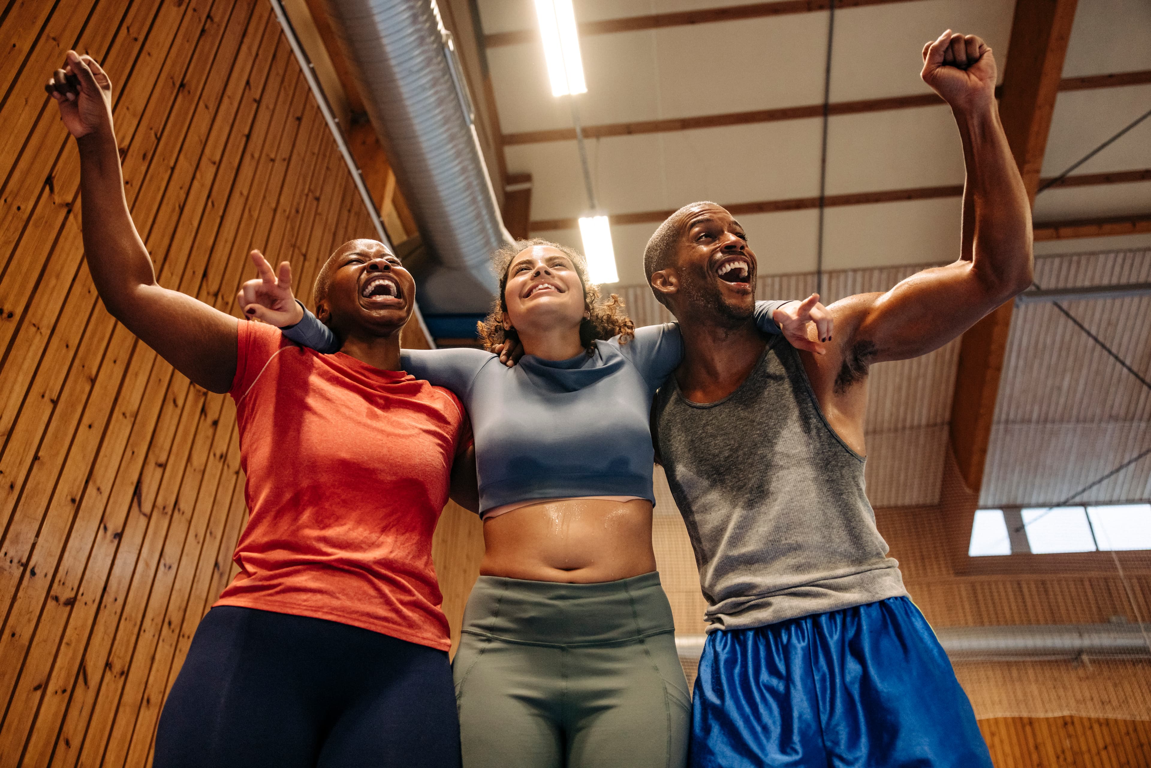 Group of 3 people cheering and smiling in a gym.