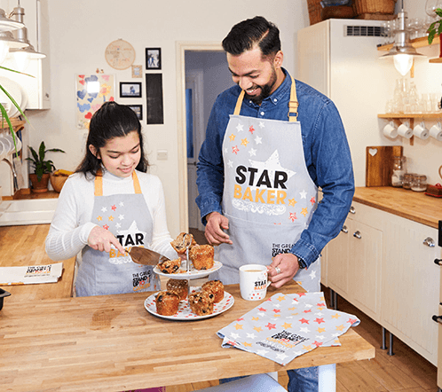 A father and daughter wearing star baker merchandise cut cake on a display.