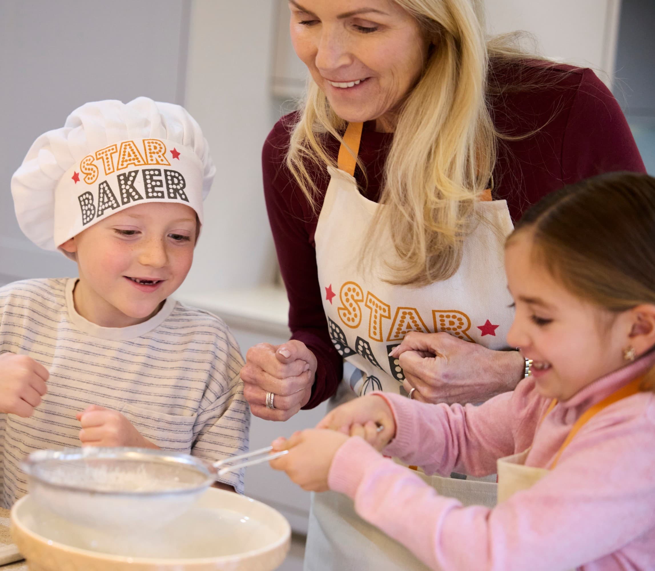 A mother, son and daughter wearing star baker merchandise baking a cake.